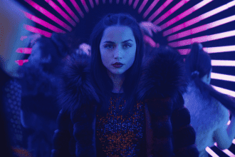Pôster de "Bailarina". personagem utilizando um casaco, em frente a luzes neon.